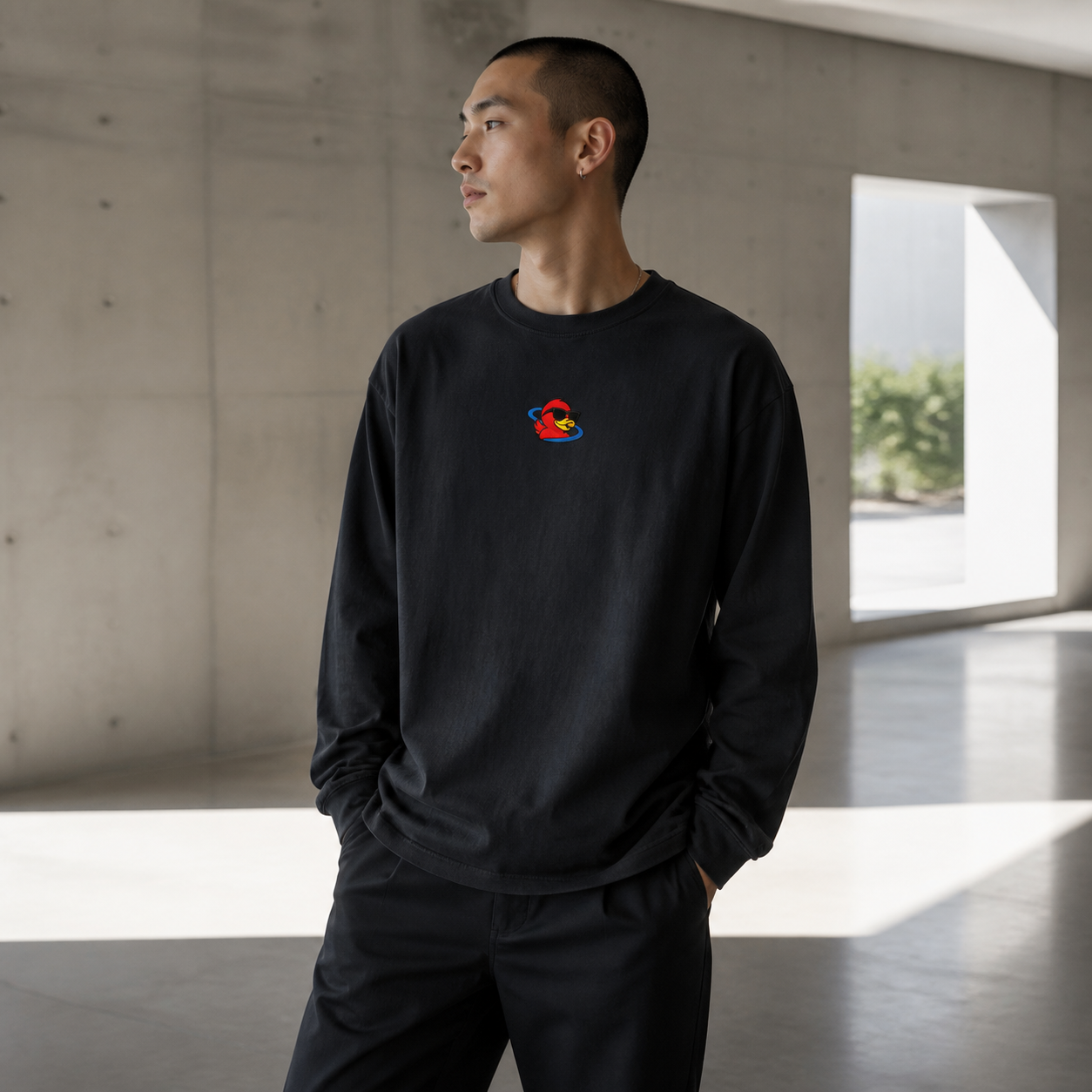 Adult wearing a minimal black long-sleeve with a small centred Cosmic Duck emblem